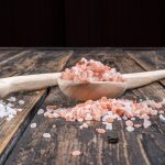 Himalayan salt in a wooden spoon and nearby side view on a dark wooden background vertical